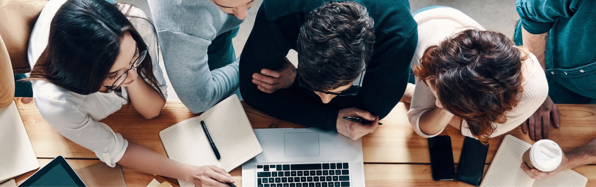 A view from above shows a work team gathered around a laptop solving a problem together