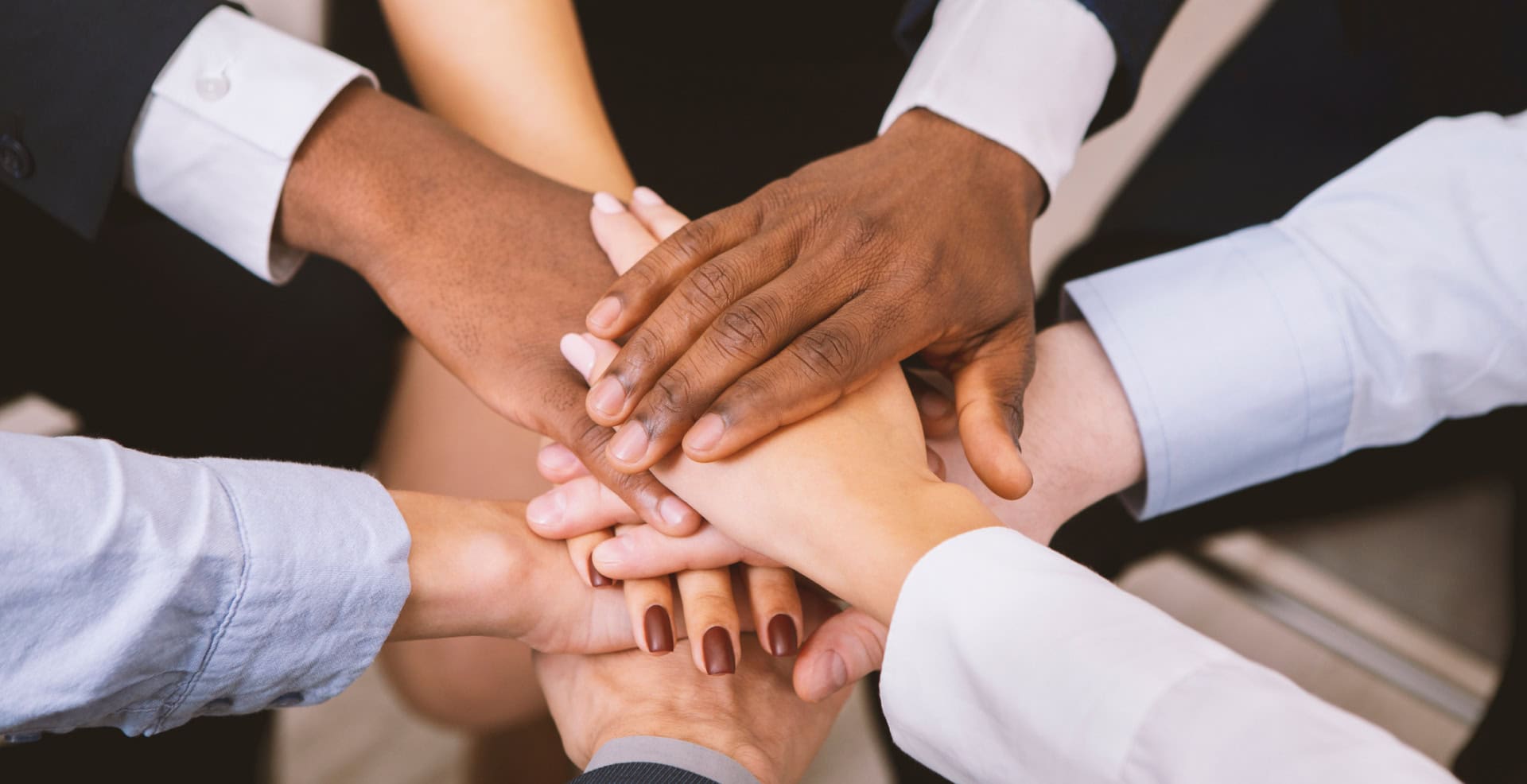 Men and women in professional attire put their hands together as a team