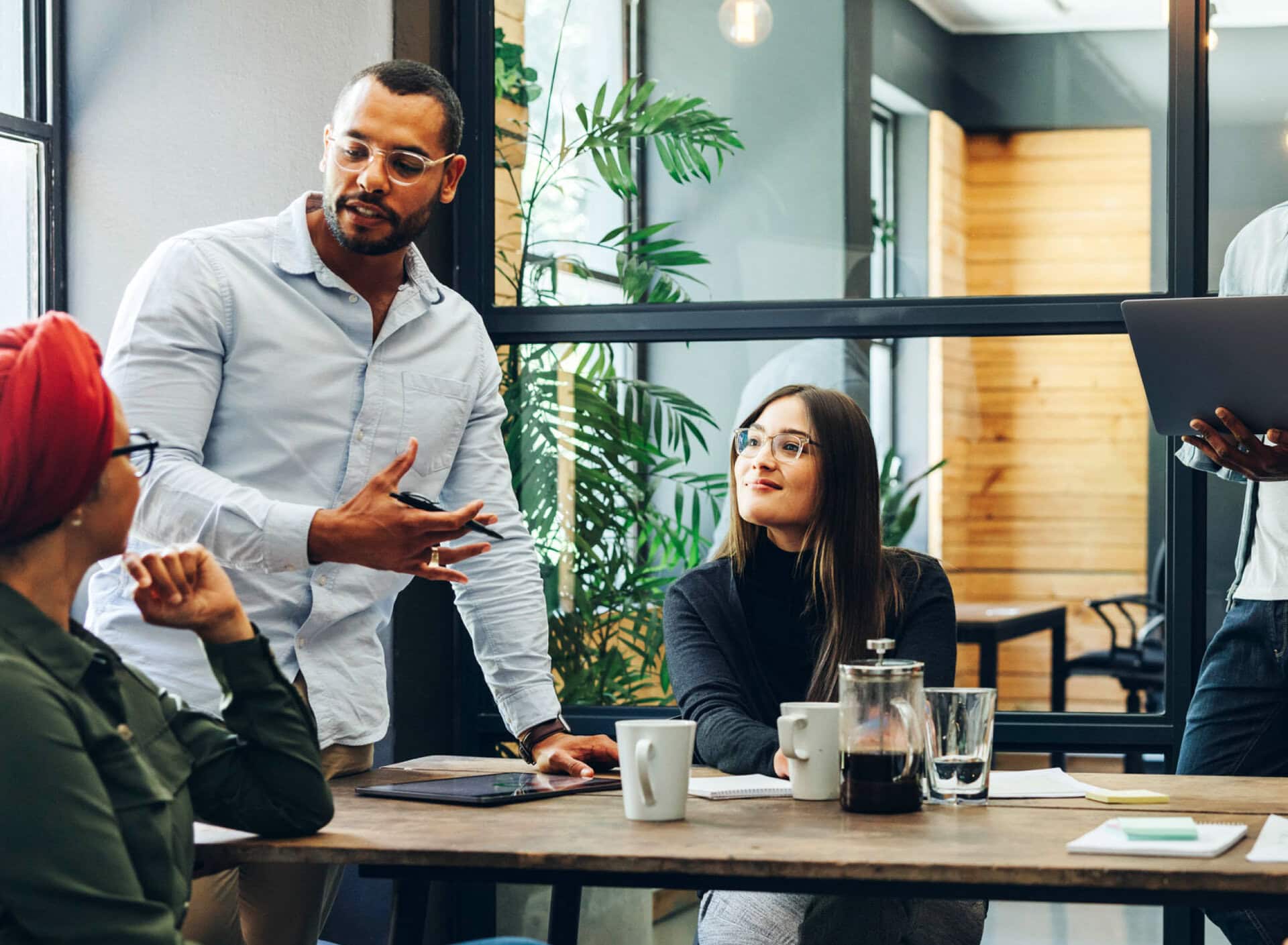 A business leader stands at a meeting table and explains something to his team