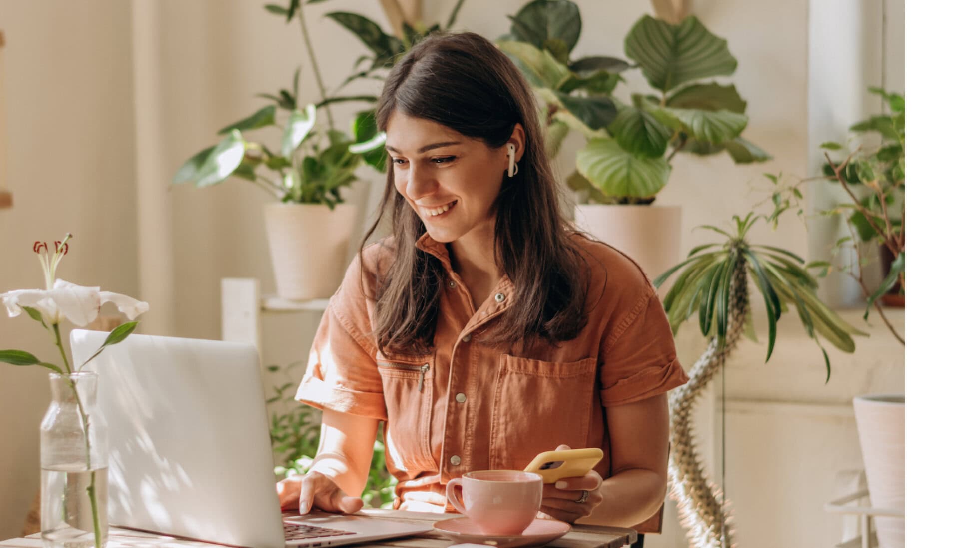 A women looks at career training options on her laptop in a bright room with plants
