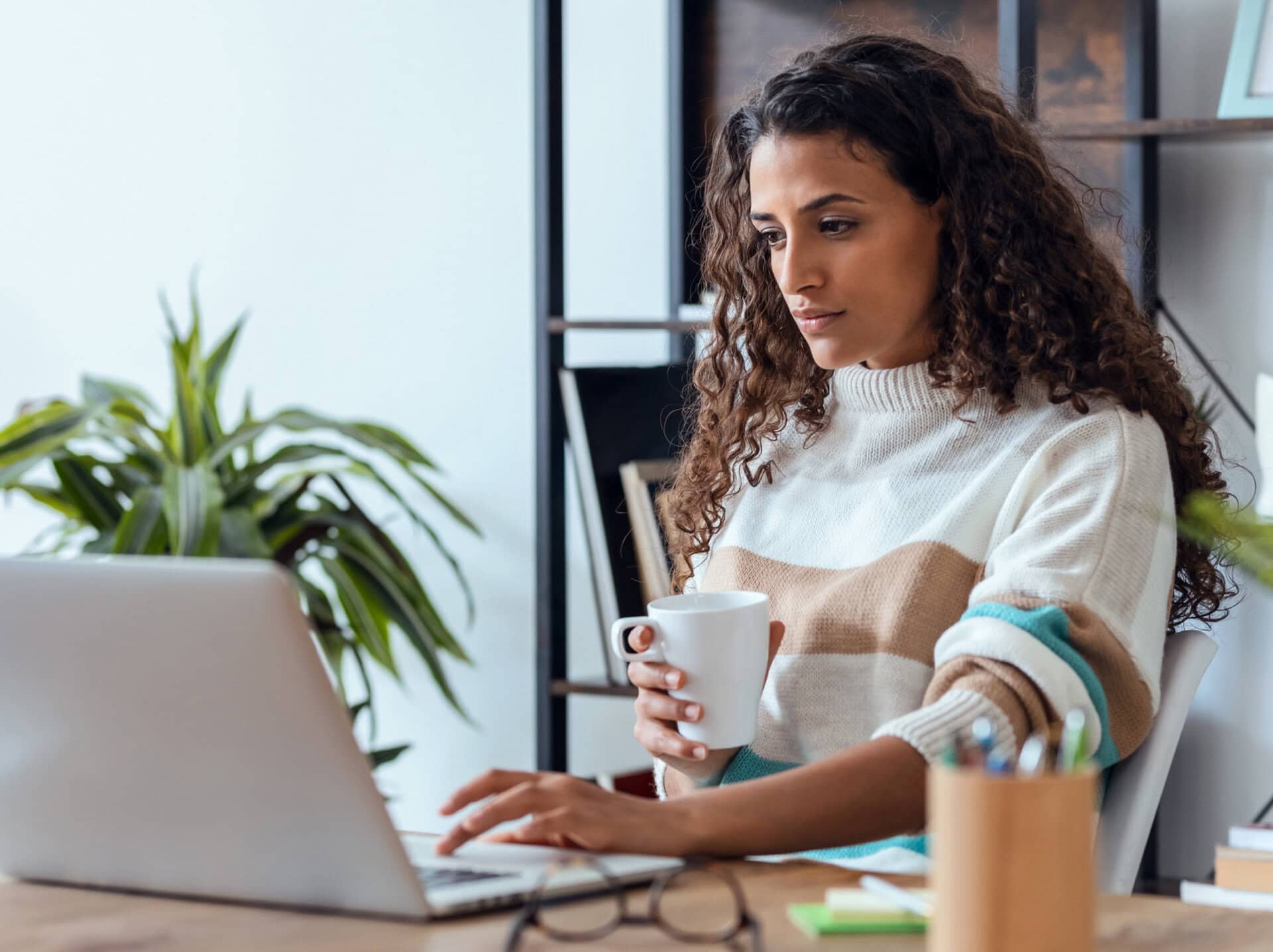 A woman with a coffee cup sits at her computer to look into job postings